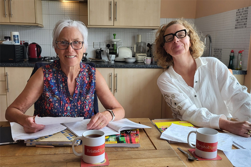 Two smiling students at desk with coursework and hot drinks